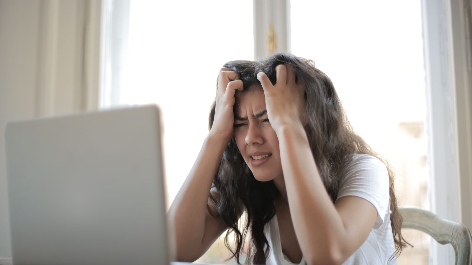 Woman at a laptop holding her head in her hands, looking frustrated