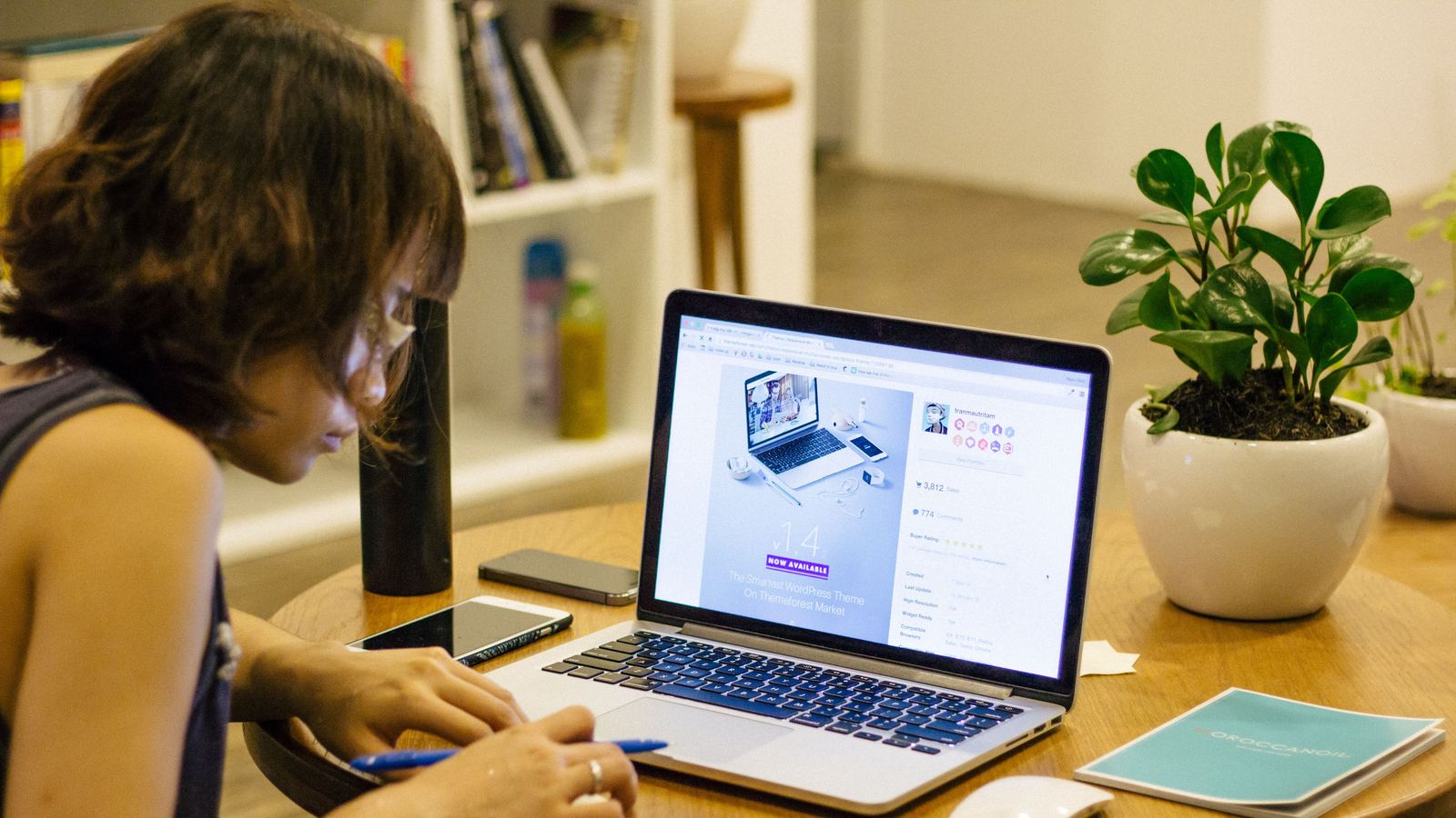 Woman working at a laptop on a round table next to a potted plant